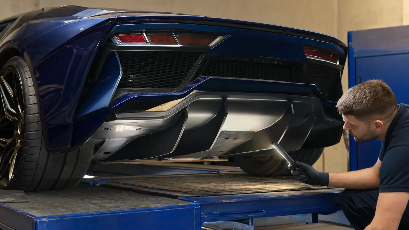 Technician inspecting the rear diffuser and lower impact path of a badge-free blue exotic car.