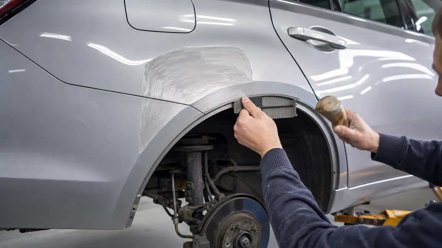Technician checking the restored contour of a rear quarter panel wheel arch before painting